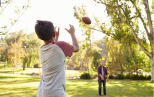 A boy tracking a football in the air preparing to catch it, thrown by his Dad.