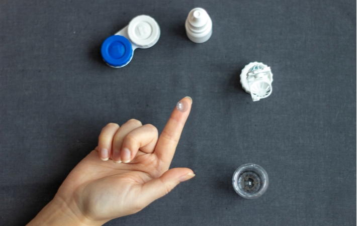 An Orthokeratology (Ortho-K) contact lens resting on a persons fingertip in front of a dark surface