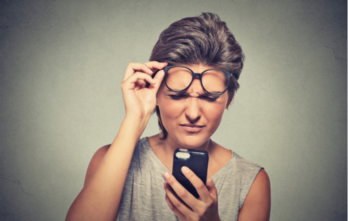A woman lifting up her glasses as she struggles to see a phone screen up close caused by possible eye conditions or diseases