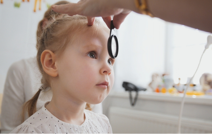 An optometrist using a tool to magnify a young girls eye's to examine them