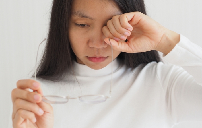A woman removing her glasses to rub her dry eyes