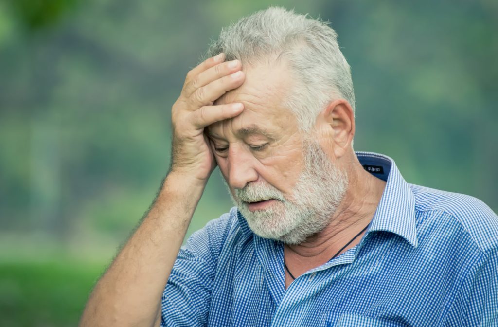 An older man with his hand on his head due to blurry vision