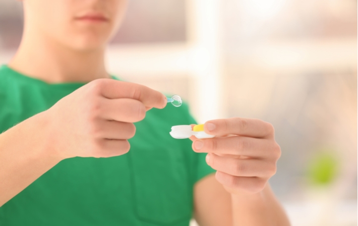 A boy with a green shirt using taking contact lenses out of their case