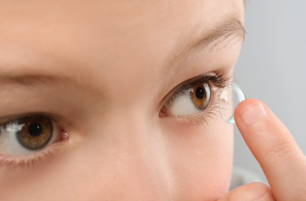 A close-up of a young child using their finger to place a contact lens in their left eye