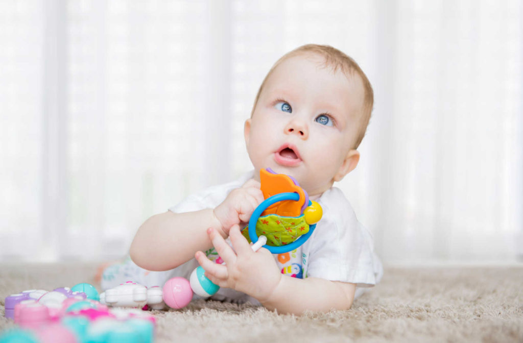 A baby laying on the floor with a toy looking up with crossed eyes