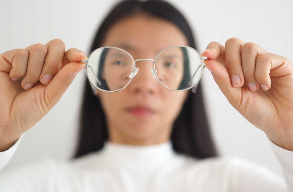 A woman with astigmatism holding out a pair of glasses